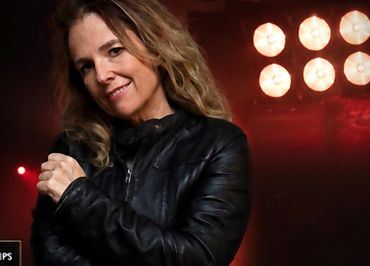 Deb Kaye, comedian, in a leather jacket under warm stage lights — smart, relatable, seriously funny